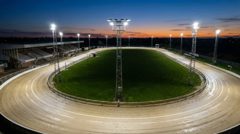 Aerial view of a UK greyhound racing track with sand surface and floodlights at dusk